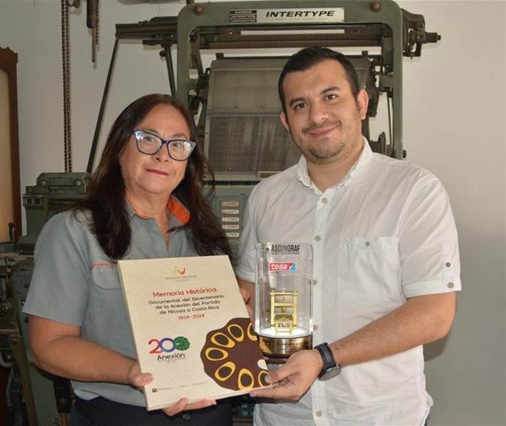 Diseñadora del libro y Director de la Imprenta sostienen una copia del libro ganador y el trofeo.